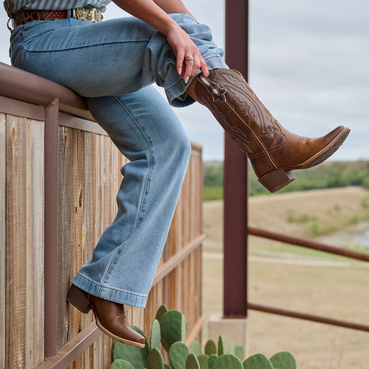 A woman pulling on a pair of cowboy boots.